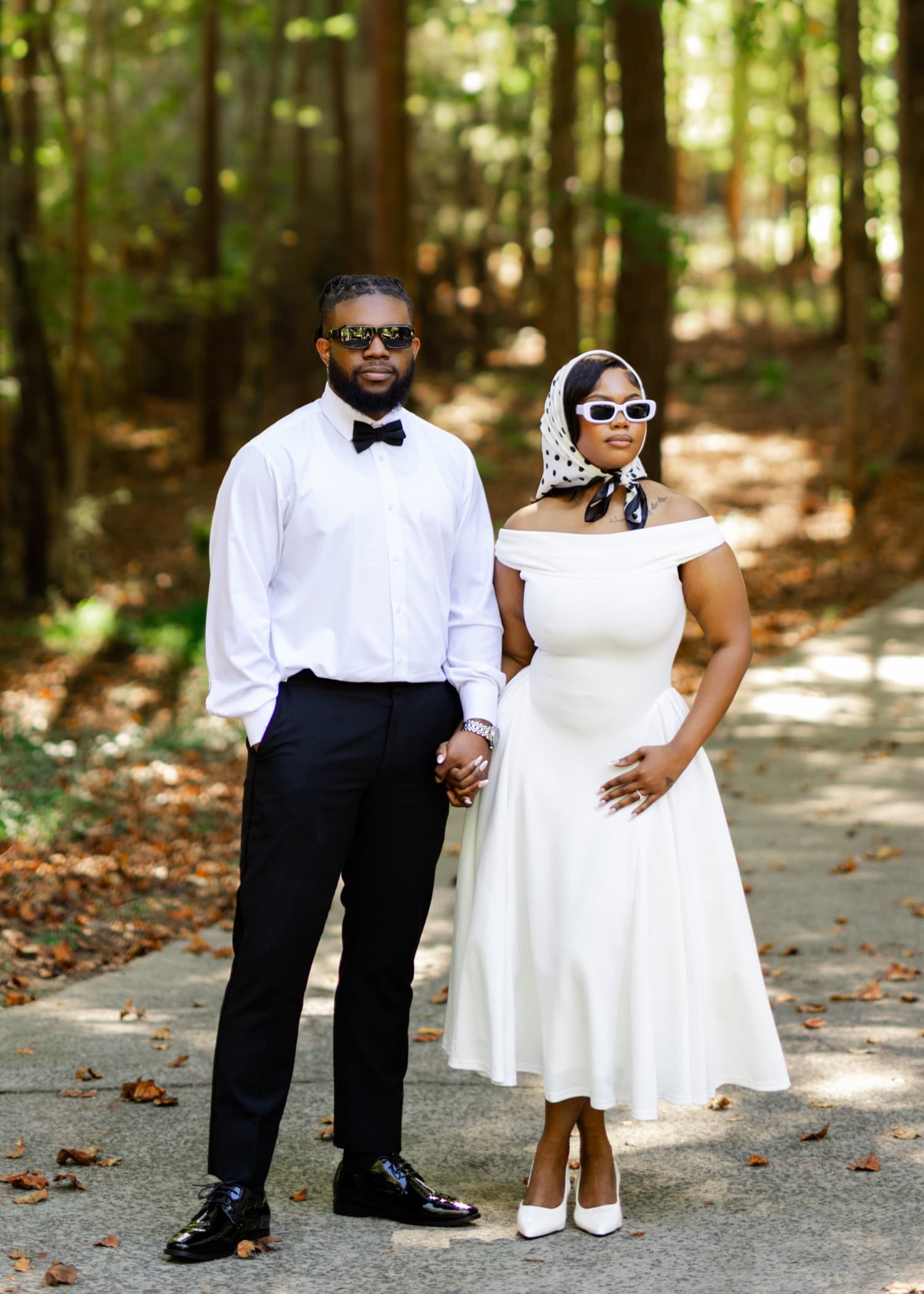 Kijori and Amoy standing hand in hand on a woodland path, he in black tie and she in a white dress and headscarf